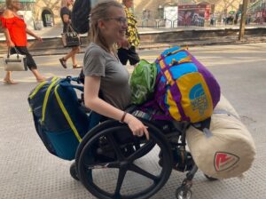 Image of Katherine - her wheelchair is loaded with bags and camping equipment