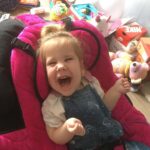 Chloe, a young girl with cerebral palsy, sits in her pink chair. She is happy and smiling.